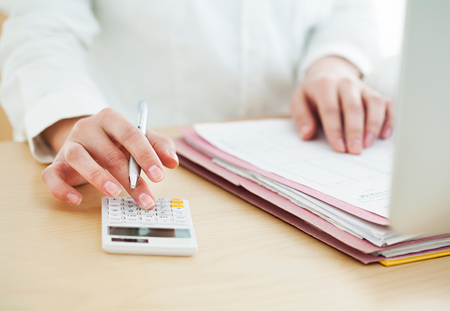 A person's hands typing on a calculator and opening a folder of documents.