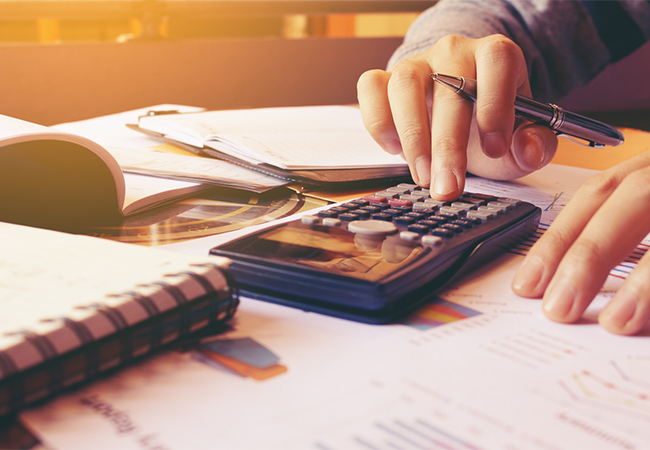 A woman's hands using a calculator near financial paperwork.