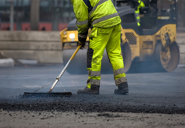 A construction worker laying asphalt on a road.