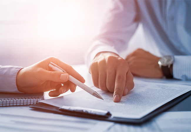 Two people sitting at a conference table, pointing at documents.