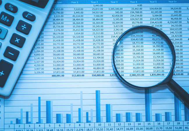 Spreadsheet of accounting documents with calculator and magnifying glass.