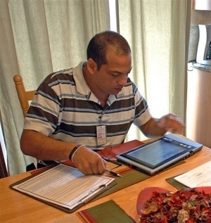 Photograph of an adjuster sitting at a table and looking at a computer tablet with a clipboard to his right.