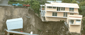 Three story house sliding down the side of a hill.