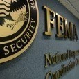 Photograph of a wall partially showing the FEMA logo. FEMA is visible to its right, with the words National and Coordination visible underneath.