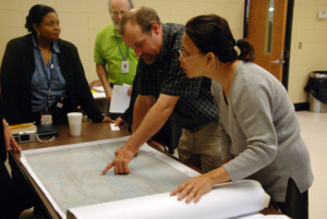 A photo of a man and a woman looking at a large map that is spread out on a table. Two people representing community officials are standing next to the table