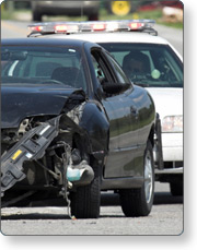A car with a smashed bumper sits in front of a police car