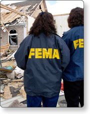 Two people wearing FEMA jackets inspecting damaged property.