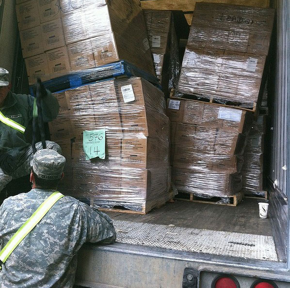 A national guard soldier looks in the back of a truck at piles of shrink-wrapped pallets of emergency food supplies.