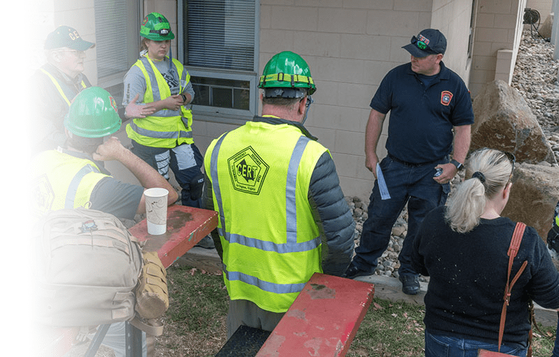 Picture of a FEMA person and multiple CERT volunteers meeting next to a building.