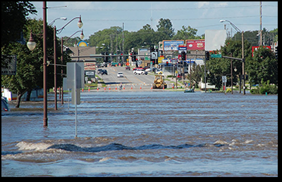 A photograph shows a shallow flood demonstrating sheet flow across a four-lane street.