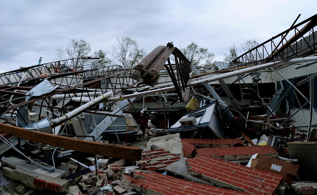 A high school has been reduced to a pile of debris with a collapsed roof, twisted structure beams and fallen brick walls.