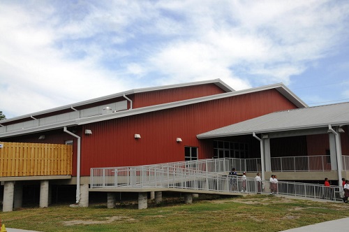 A multipurpose building elevated on pylons with a long, railed ramp leading to a covered entrance.