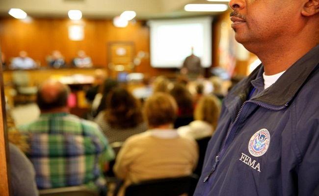 FEMA Applicant Briefing with an individual in the foreground wearing a FEMA jacket.