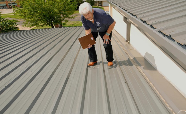 FEMA Public Assistance Officer and member of a Preliminary Damage Assessment team sights down a metal roof to gauge the damage caused by hail from a tornado.