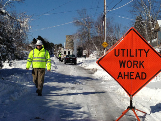 Utility workers repair downed power lines following the Northeast Blizzard. A sign reads Utility Work Ahead.