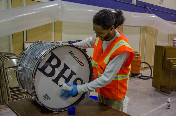 A person cleaning a marching bass drum at Beach Haven school after flooding.