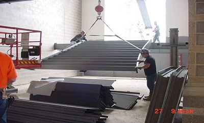 Construction workers steadying prefabricated stairs as a crane lowers them into place.