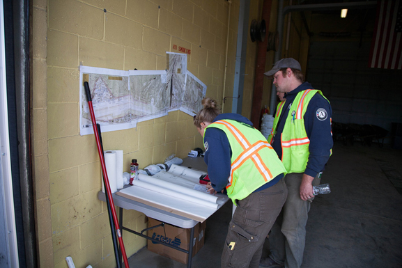 Workers in safety vests consult project plans at a work site in Galena, AK.