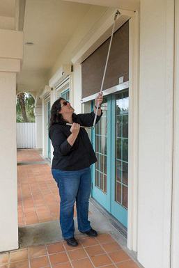 A woman rolling down a hurricane shutter over a pair of French doors.