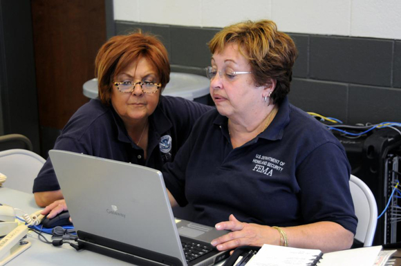 Two FEMA specialists work together at a laptop.