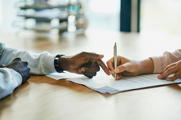 A contract being talked over with one person's hands on the left and another person on the right with a pen