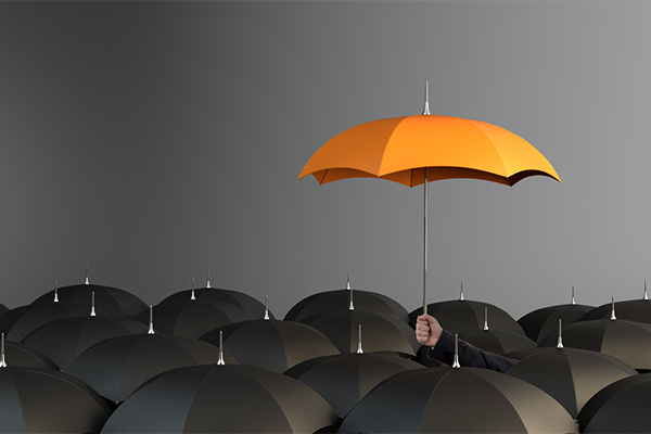 The tops of many black umbrellas with one person holding up an orange umbrella