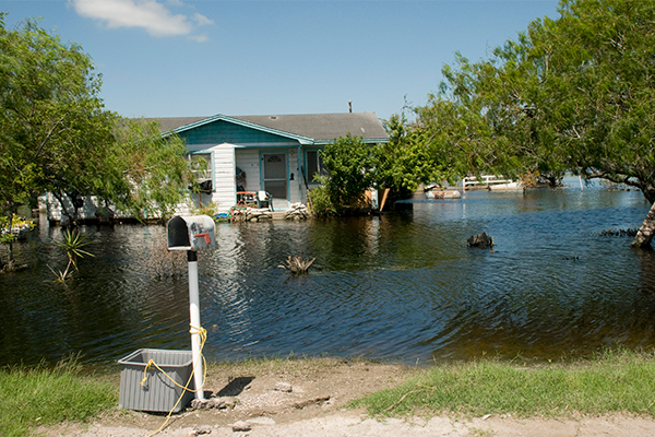 A flooded single level home surrounded by flood water and trees