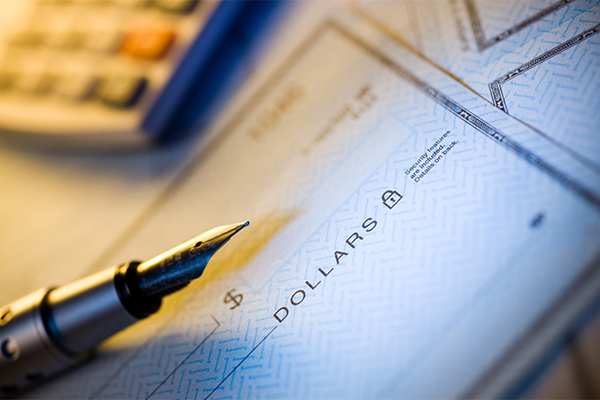 Closeup of a blank check with a pen over it and a calculator in the background