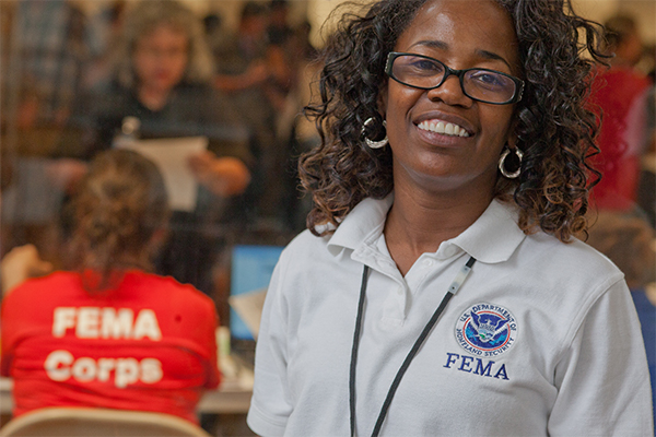 A FEMA specialist standing and smiling in the foreground with people in the background.