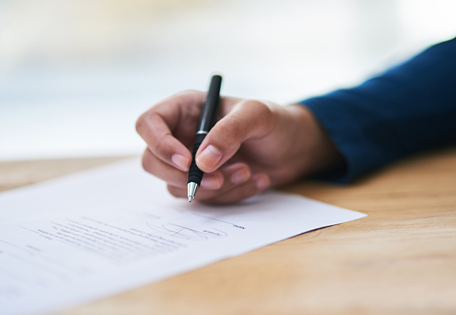 A person's hand signing a document with a pen