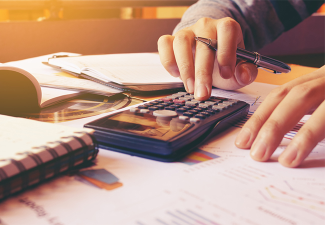 A woman's hands using a calculator, with financial documents spread out on a desk.