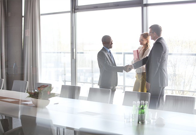 Three business people shake hands near a conference table.