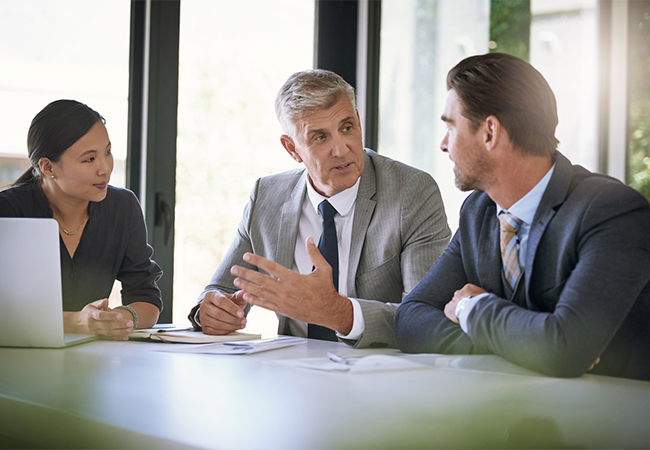 Three business people sitting at a conference table, having a discussion.