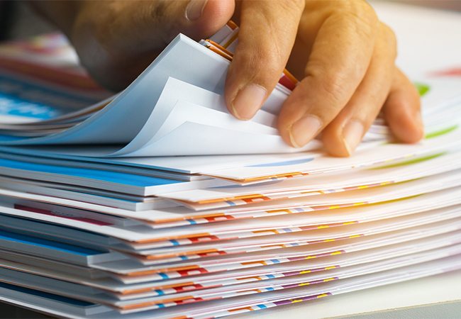 A man's hands leafing through a stack of documents.