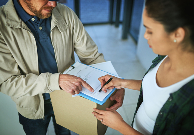 Delivery man holding out a document on a clipboard for a business woman.