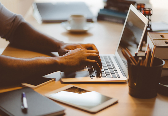 A man's hands typing on a laptop at a desk.