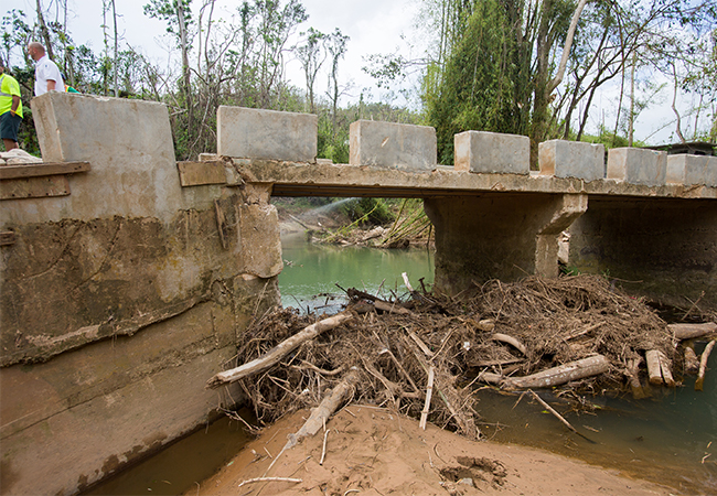 Debris piled up against bridge supports in a stream.