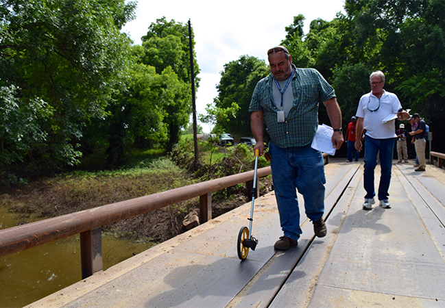 Two FEMA PA workers measuring damage to a bridge while one records the data.