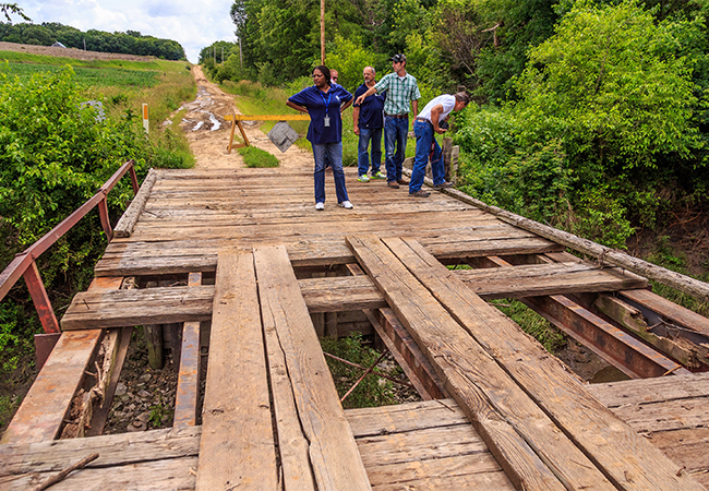 A Preliminary Damage Assessment Team looking at a wooden bridge that was damaged by heavy rain.