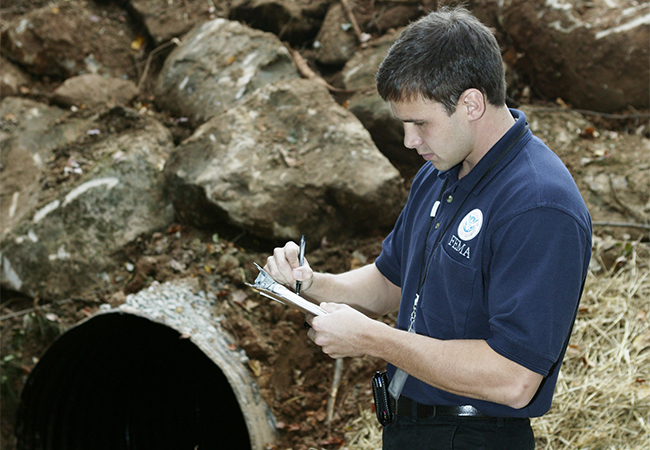 FEMA Public Assistance Specialist in Georgia reviewing a document by a bridge and culvert.