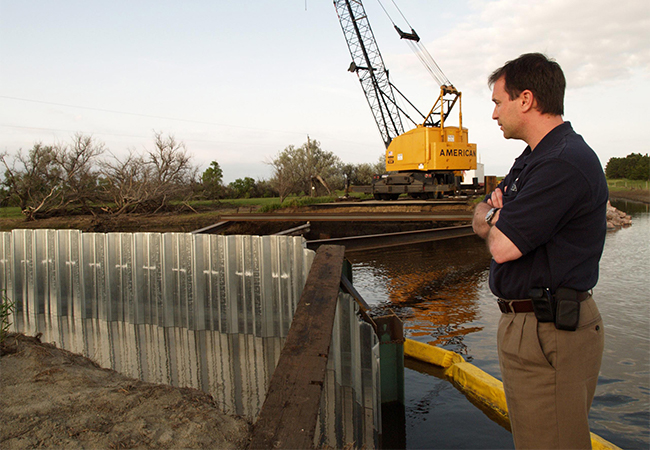 A FEMA FCO looking at a destroyed bridge with construction equipment in the background.