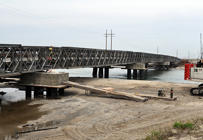 An almost completed new inlet bridge on a beach with construction equipment.