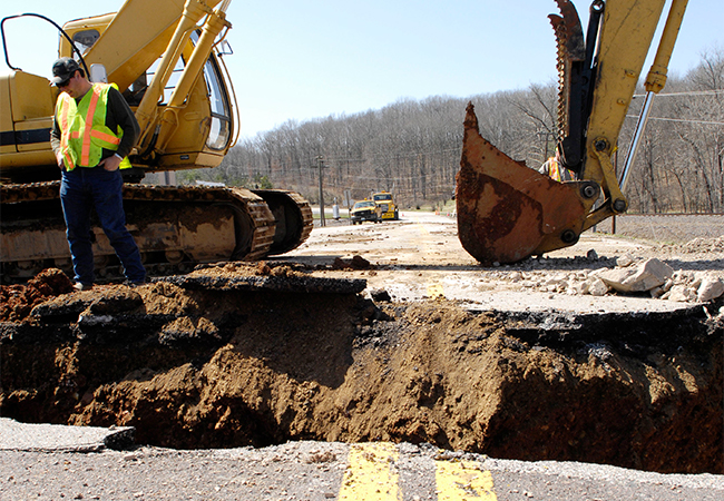 Construction worker and equipment on a severely flood-damaged bridge.