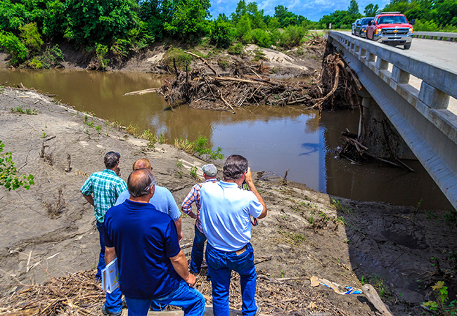 A Preliminary Damage Assessment Team looking at a stream with debris under a bridge.