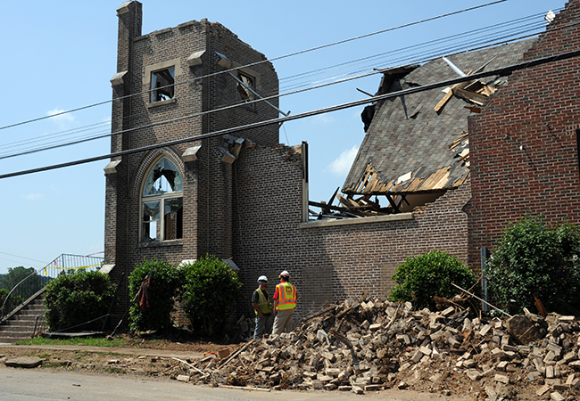 Contractors outside a heavily damaged brick church with debris.