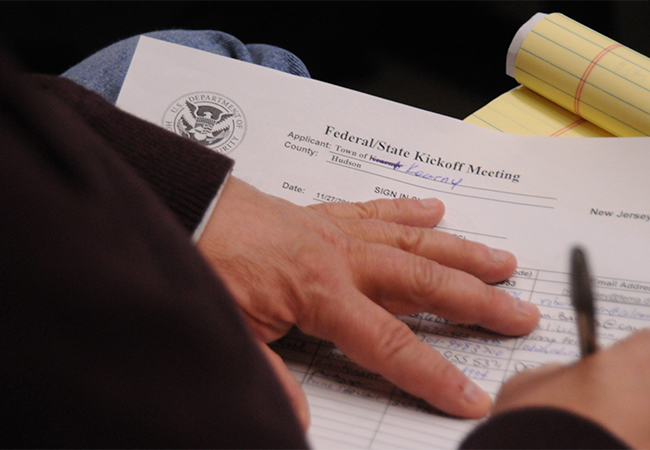 A person's hand writing on the Federal/State Recovery Scoping  Meeting sign-in sheet