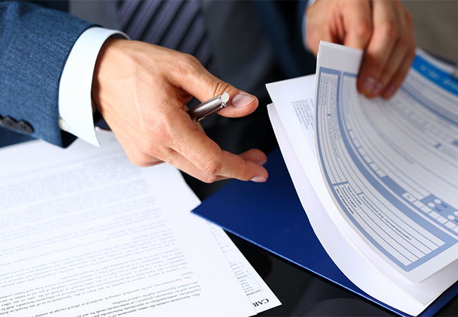 Person's hand sorting through insurance forms on a clipboard