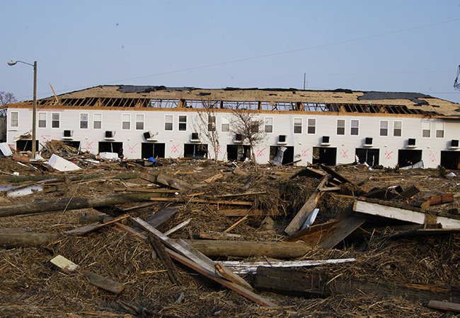 A heavily damaged housing building complex with debris all around.