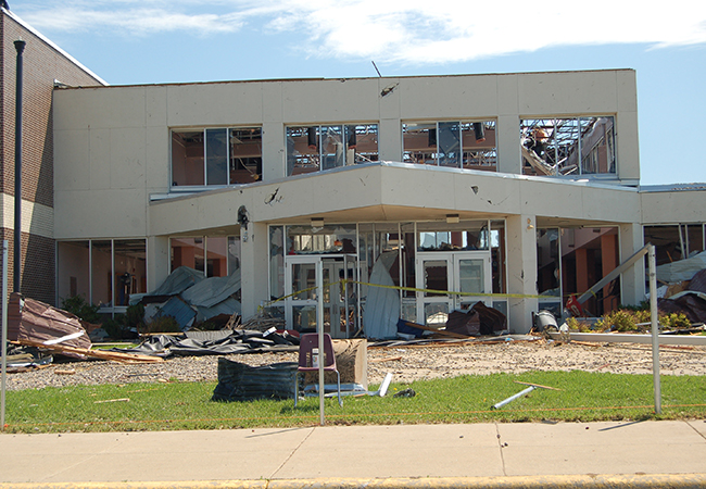 A heavily damaged school from a tornado with yellow caution tape outside.