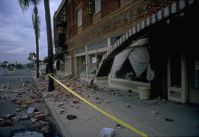 Damaged buildings with yellow caution tape and debris on the street.